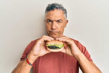 Handsome middle age mature man eating a tasty classic burger skeptic and nervous, frowning upset because of problem. negative person.