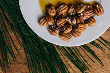 A white plate of Georgia pecans drizzled with local honey and powdered sugar on a wood charcuterie board