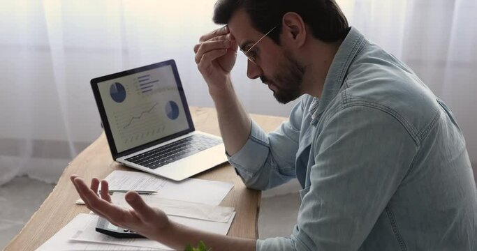 Serious man sit at desk with laptop, graphs charts on device screen, do accounting work feels stressed search mistake in calculations. Debt, loss, individual entrepreneur business bankruptcy concept
