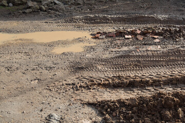muddy broken road made of earth and clay without asphalt with large muddy puddles, bricks, tire marks close-up