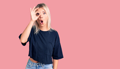 Young beautiful blonde woman wearing casual t-shirt doing ok gesture shocked with surprised face, eye looking through fingers. unbelieving expression.