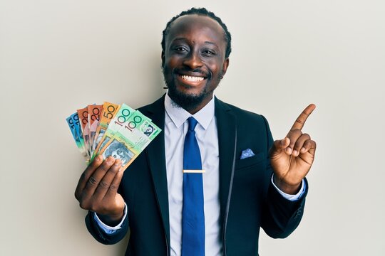 Handsome young black man wearing business suit and tie holding australian dollars smiling happy pointing with hand and finger to the side
