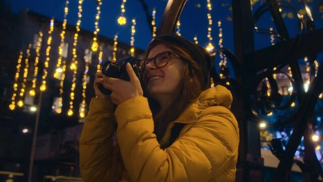 Excited travel blogger makes photos with professional photo camera of night street with holiday festive lights. Festive mood and inspiration. Traveling in christmas winter times. Cinematic video