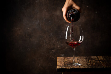 Pouring red wine into the glass against rustic dark wooden background