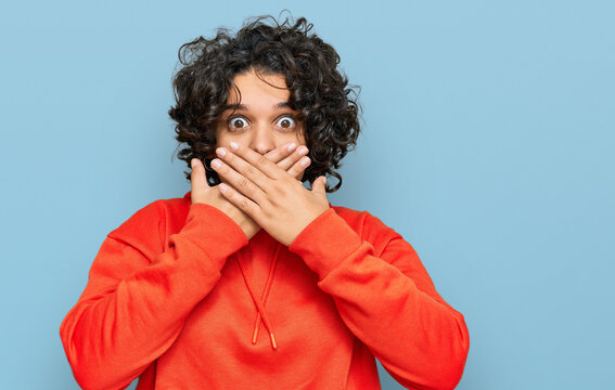 Young hispanic woman with curly hair wearing casual sweatshirt shocked covering mouth with hands for mistake. secret concept.