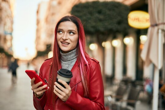 Young caucasian girl smiling happy using smartphone and drinking coffee at the city.