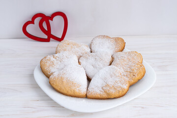 Heart-shaped cookies decorated for Valentine's Day.Cookies on a white plate on a white wooden background.The concept of the Valentine's Day holiday.