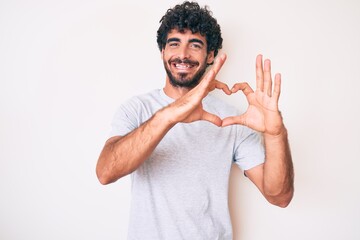 Fototapeta premium Handsome young man with curly hair and bear wearing casual tshirt smiling in love showing heart symbol and shape with hands. romantic concept.
