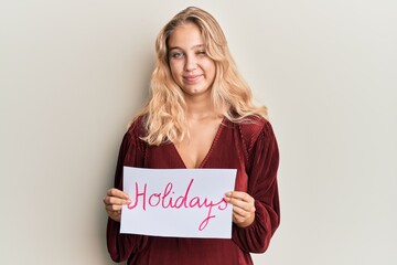 Young blonde girl holding holidays banner message winking looking at the camera with sexy expression, cheerful and happy face.