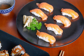 Salmon sushi typical of Japanese cuisine on black plate, natural light inside restaurant