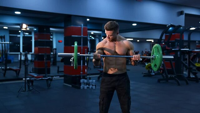 Athletic man in gym exercising with barbell. Bodybuilder with perfect body. Naked torso with perfect abs.