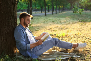 Obraz premium Young man reading book on green grass near tree in park