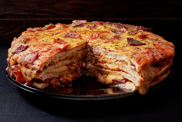 Italian Pizza Cake with four layers full of grilled salami, ham and moose sausage. Black background.