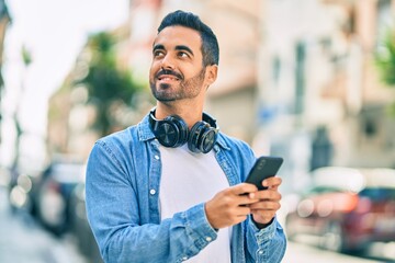 Young hispanic man smiling happy using smartphone and headphones at the city.