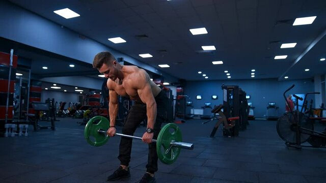 Fit young man lifting barbells doing workout at a gym. Sport, fitness, weightlifting, bodybuilding, training, athlete, workout exercises concept. View from the side.