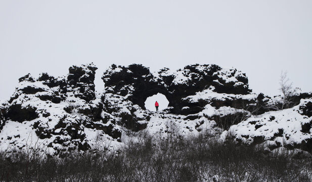 Tourist person red jacket standing in hole window of Dimmuborgir volcanic lava fields rock formation Myvatn Iceland