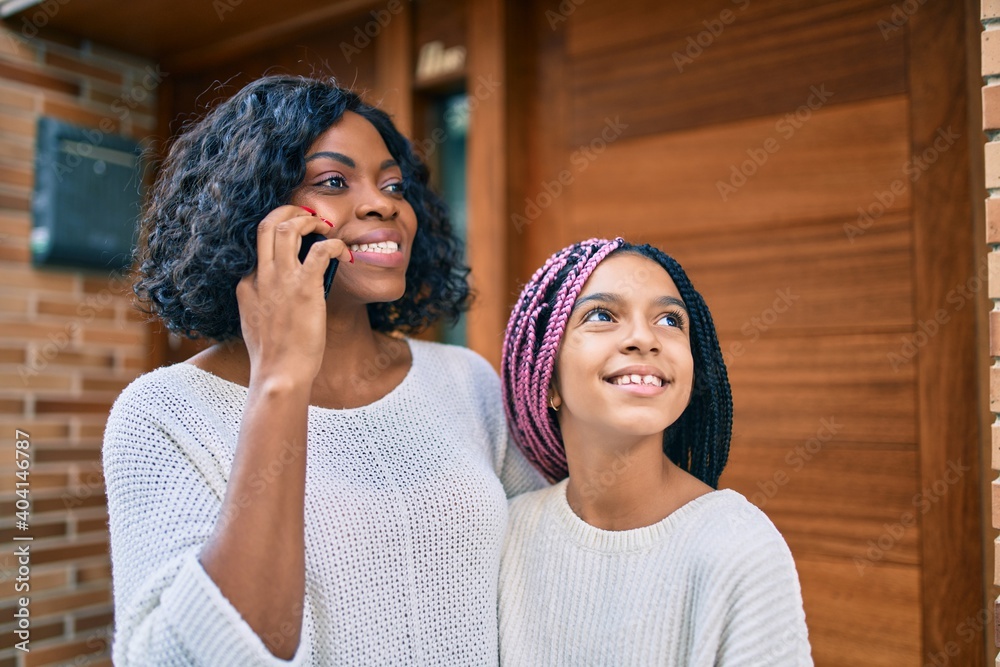 Poster african american mother and daugther hugging and talking on the smartphone at the city.