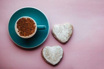 flat lay of cup of fresh morning cappuccino sprinkled with cocoa powder on top and homemade ginger cookies in the shape of heart. on pink backdrop. concept of Valentine day and romantic.