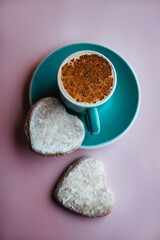 cup of fresh morning cappuccino sprinkled with cocoa powder on top and homemade ginger cookies in the shape of heart. on pink backdrop. concept of Valentine day and romantic breakfast.  Blogger style.