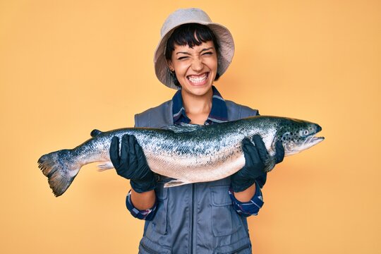 Beautiful brunettte fisher woman showing raw salmon smiling and laughing hard out loud because funny crazy joke.