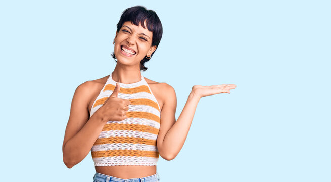Young brunette woman with short hair wearing casual clothes showing palm hand and doing ok gesture with thumbs up, smiling happy and cheerful