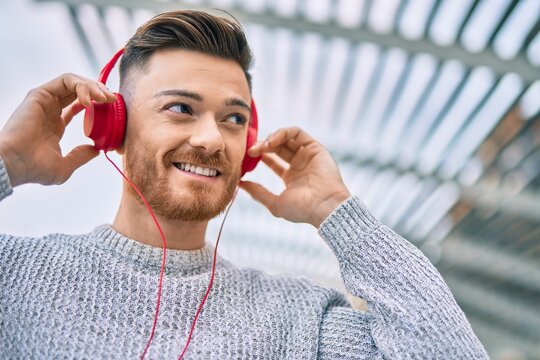 Young caucasian man smiling happy listening to music using headphones at the city.