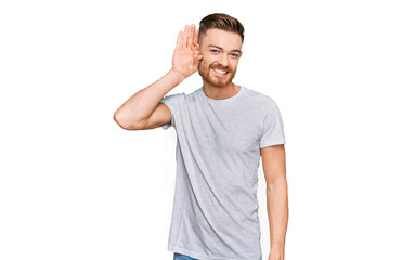 Young redhead man wearing casual grey t shirt smiling with hand over ear listening an hearing to rumor or gossip. deafness concept.