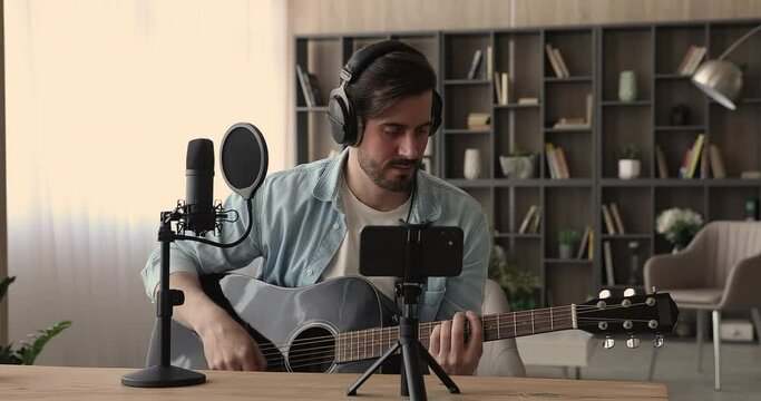 Guitarist wear headphones participate in live stream play guitar put cellular on tripod record video while sing song perform string instrument play. Tutorial class for internet auditory, hobby concept