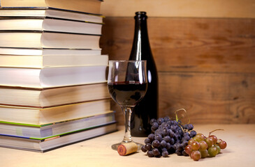 A glass of red wine with grapes, books and bottle