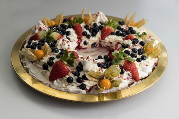Delicious pavlova cake wreath of french meringue and whipped cream, decorated with strawberry, blueberries and physalis, view from above