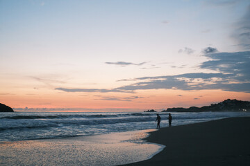 Atardecer en playa de Ixtapa Zihuatanejo, Mexico, atardecer en tono naranja y azul con un par de siluetas sobre la arena y cerca del mar. 