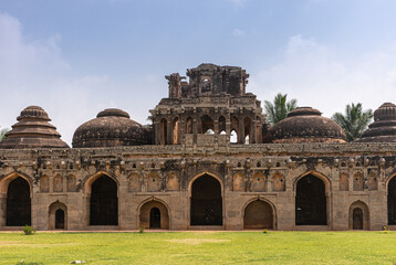 Hampi, Karnataka, India - November 5, 2013: Zanana Enclosure. Central part of Brown stone ruinous Elephant stables with multiple domes seen over green lawn under blue cloudscape. 