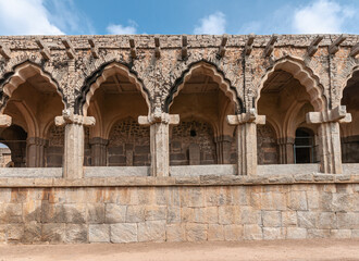 Fototapeta premium Hampi, Karnataka, India - November 5, 2013: Zanana Enclosure. Facade of arches at archeological items brown-stone exhibition hall under blue cloudscape