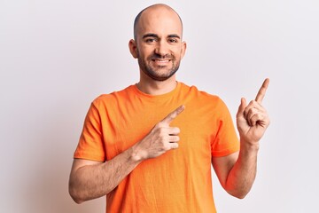 Fototapeta premium Young handsome bald man wearing casual t shirt smiling and looking at the camera pointing with two hands and fingers to the side.