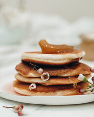 Delicious and hearty breakfast. Pancakes are stacked on top of each other with white flowers between them, pancakes topped with apricot jam. The jam is dripping over the pancakes. Flowers in food.