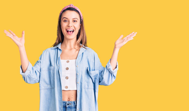 Young beautiful girl wearing casual shirt and diadem celebrating victory with happy smile and winner expression with raised hands
