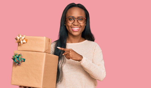 Young black woman holding gifts smiling happy pointing with hand and finger