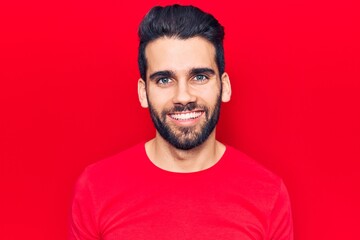 Obraz premium Young handsome man with beard wearing casual t-shirt looking positive and happy standing and smiling with a confident smile showing teeth