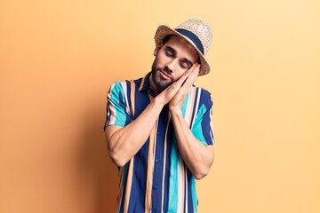 Young handsome man with beard wearing summer hat and shirt sleeping tired dreaming and posing with hands together while smiling with closed eyes.