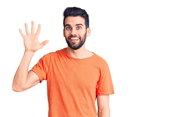 Young handsome man with beard wearing casual t-shirt showing and pointing up with fingers number five while smiling confident and happy.