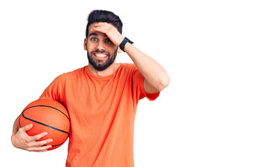 Fototapeta premium Young handsome man with beard hoilding basketball ball stressed and frustrated with hand on head, surprised and angry face