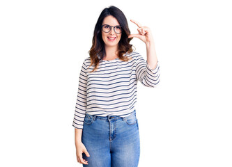 Beautiful young brunette woman wearing casual clothes and glasses smiling and confident gesturing with hand doing small size sign with fingers looking and the camera. measure concept.
