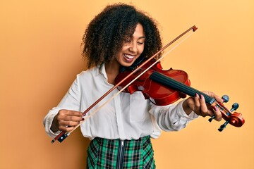Beautiful african american woman with afro hair playing classical violin smiling and laughing hard out loud because funny crazy joke. © Krakenimages.com