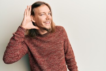 Handsome caucasian man with long hair wearing casual winter sweater smiling with hand over ear listening and hearing to rumor or gossip. deafness concept.