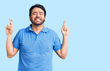 Fototapeta premium Young hispanic man wearing casual clothes gesturing finger crossed smiling with hope and eyes closed. luck and superstitious concept.