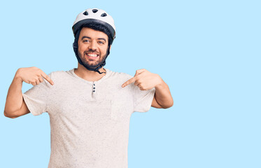 Young hispanic man wearing bike helmet looking confident with smile on face, pointing oneself with fingers proud and happy.