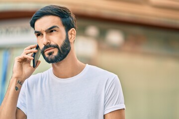 Young hispanic man with serious expression talking on the smartphone at the city.