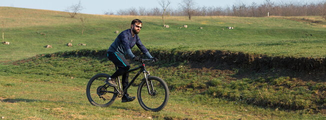 Cyclist in shorts and jersey on a modern carbon hardtail bike with an air suspension fork standing on a cliff against the background of fresh green spring forest