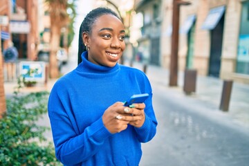 Young african american woman smiling happy using smartphone at the city.