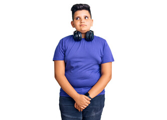 Little boy kid listening to music wearing headphones smiling looking to the side and staring away thinking.